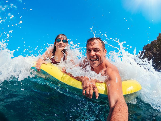Father and daughter floating on yellow tube and having fun on the beach while getting splashed by the wave