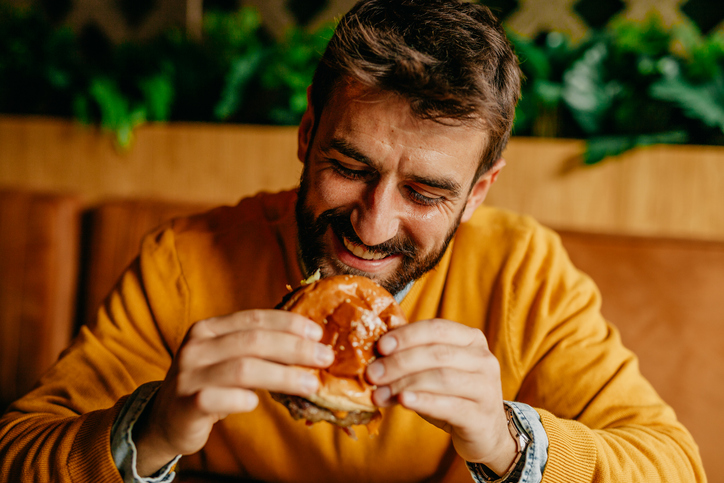 Cool looking close up of a handsome looking bearded young adult guy eating the best burger in myrtle beach